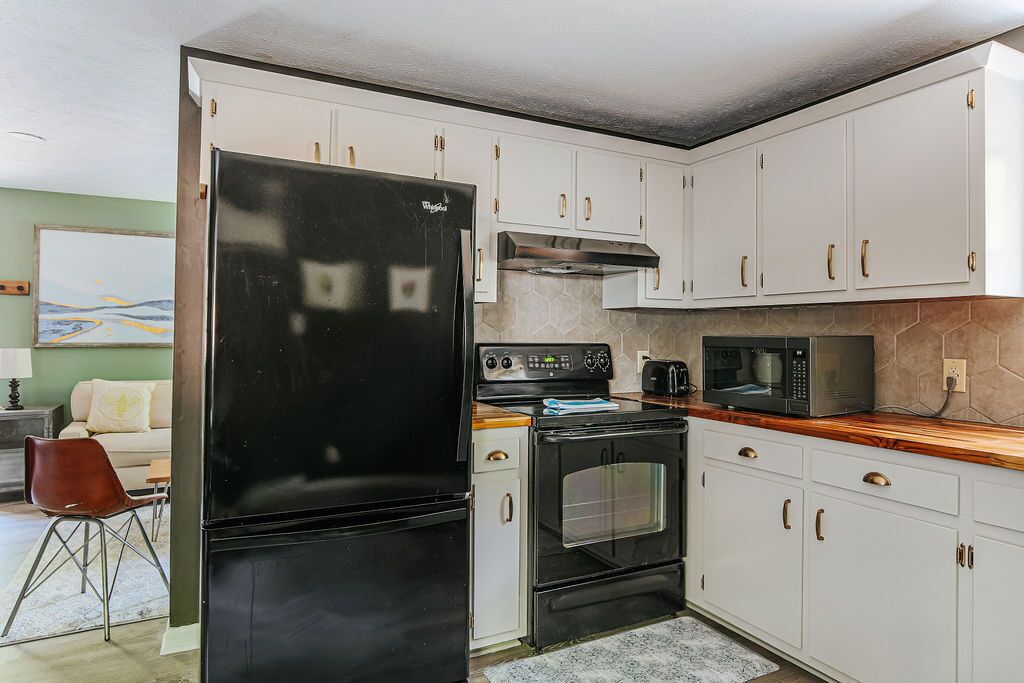 A compact kitchen with white cabinets, a black refrigerator, a microwave, and a stove.