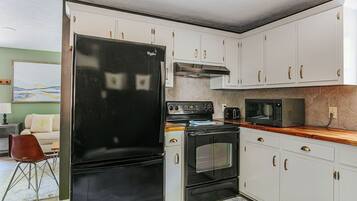 A compact kitchen with white cabinets, a black refrigerator, a microwave, and a stove.