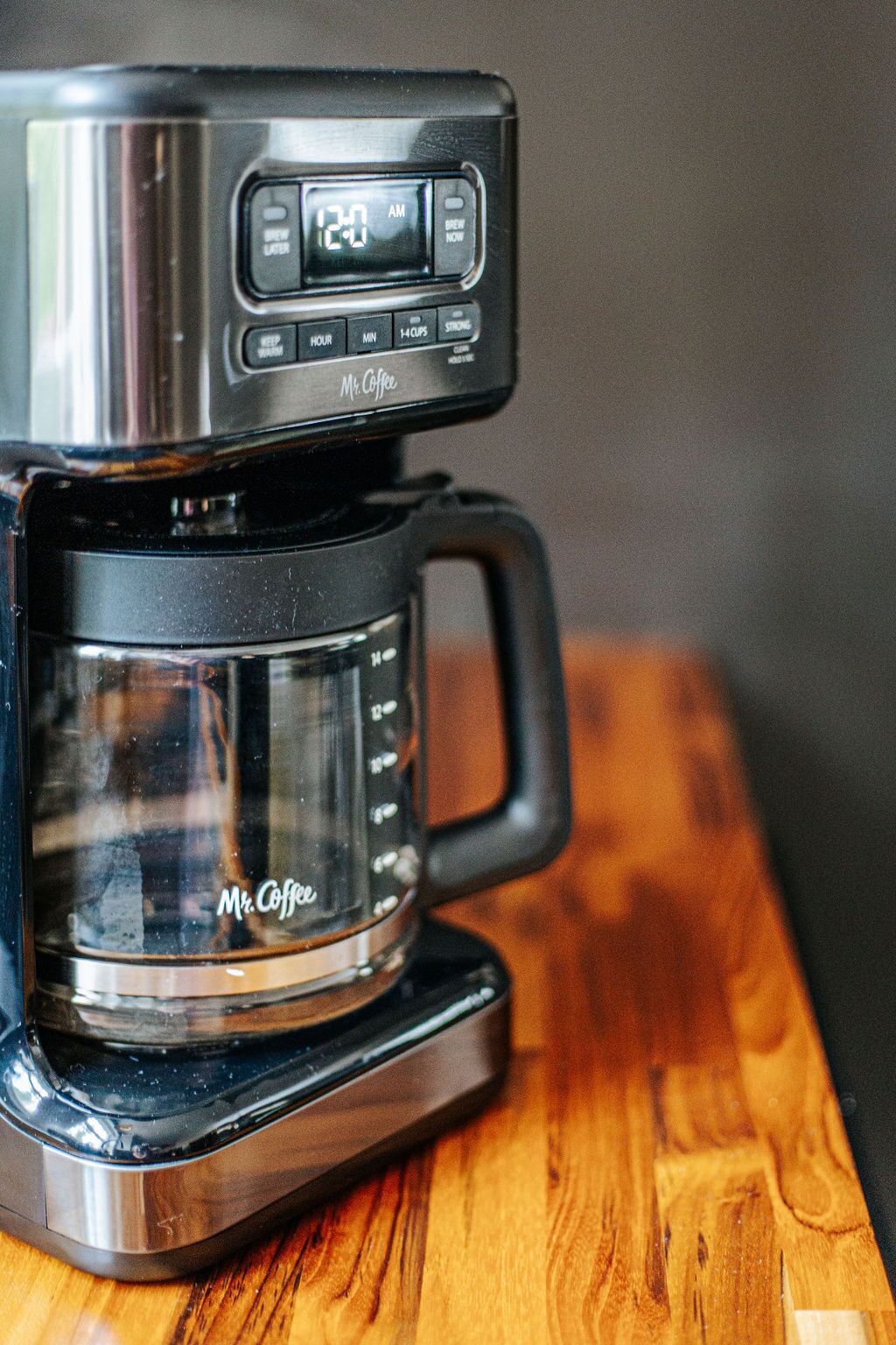 A coffee maker with a digital clock displaying 12:04 AM, a glass carafe, and a wooden table.