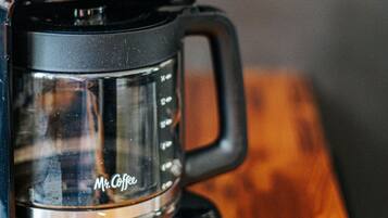 A coffee maker with a digital clock displaying 12:04 AM, a glass carafe, and a wooden table.