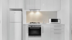 Moderni keittiö, jossa on valkoiset kaapit, sisäänrakennettu uuni, mikroaaltouuni ja jääkaappi.