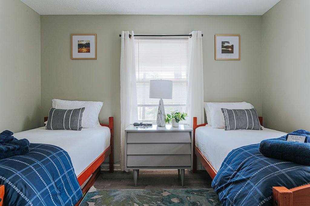 Quarto com duas camas, uma escrivaninha e uma janela com cortinas.