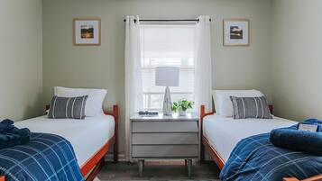 Quarto com duas camas, uma escrivaninha e uma janela com cortinas.
