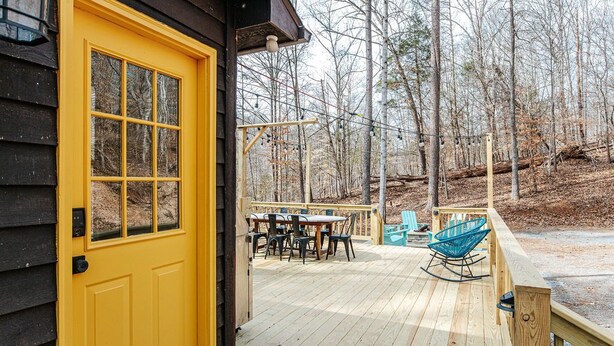 A wooden deck with a yellow door, a table with chairs, and a rocking chair. - Tucked Inn: Upper Unit (Nellysford)