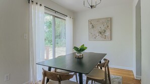 Un comedor con una mesa negra, dos sillas de madera, una planta en maceta, un candelabro y un cuadro abstracto grande en la pared.