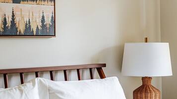 Una cama bien tendida con sábanas blancas, un cabecero de madera y un cuadro de paisaje enmarcado encima.