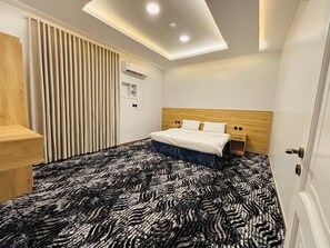 Habitación de hotel con cama, escritorio, armario, lámpara de techo y aire acondicionado.