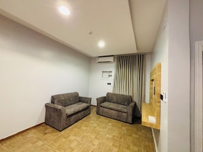 A room with two sofas, a wooden floor, an air conditioning unit, and a wooden shelf. - اونارا ستاي 2 للشقق المخدومه (Madinah)