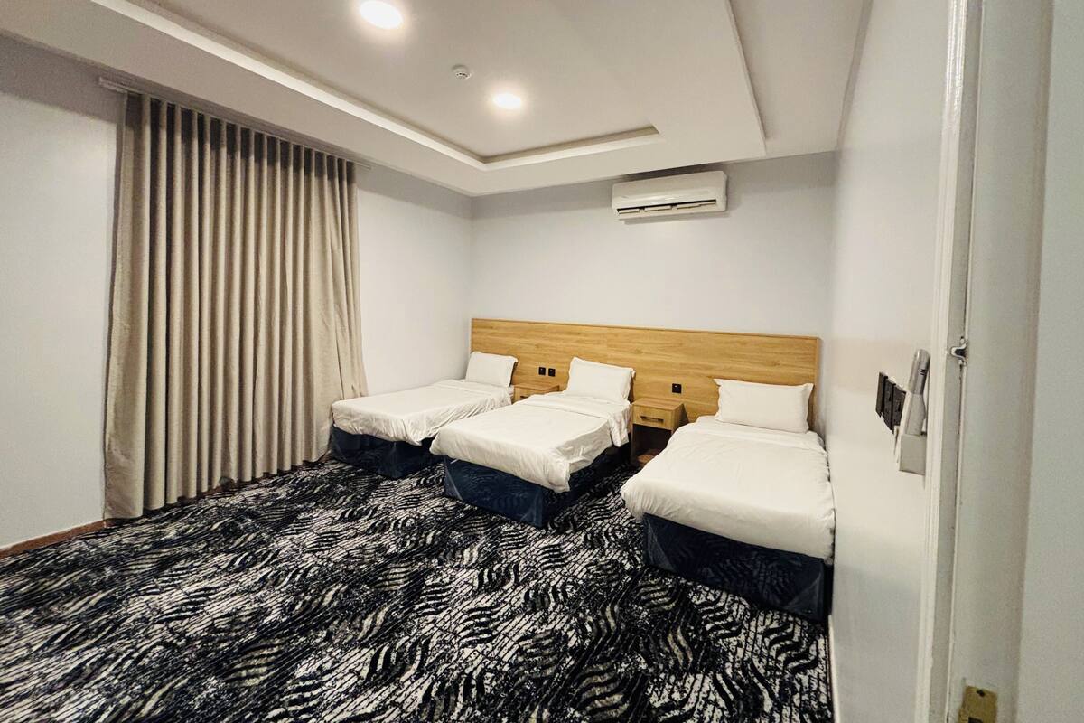 A hotel room with two beds, a patterned carpet, a ceiling light, and an air conditioning unit.