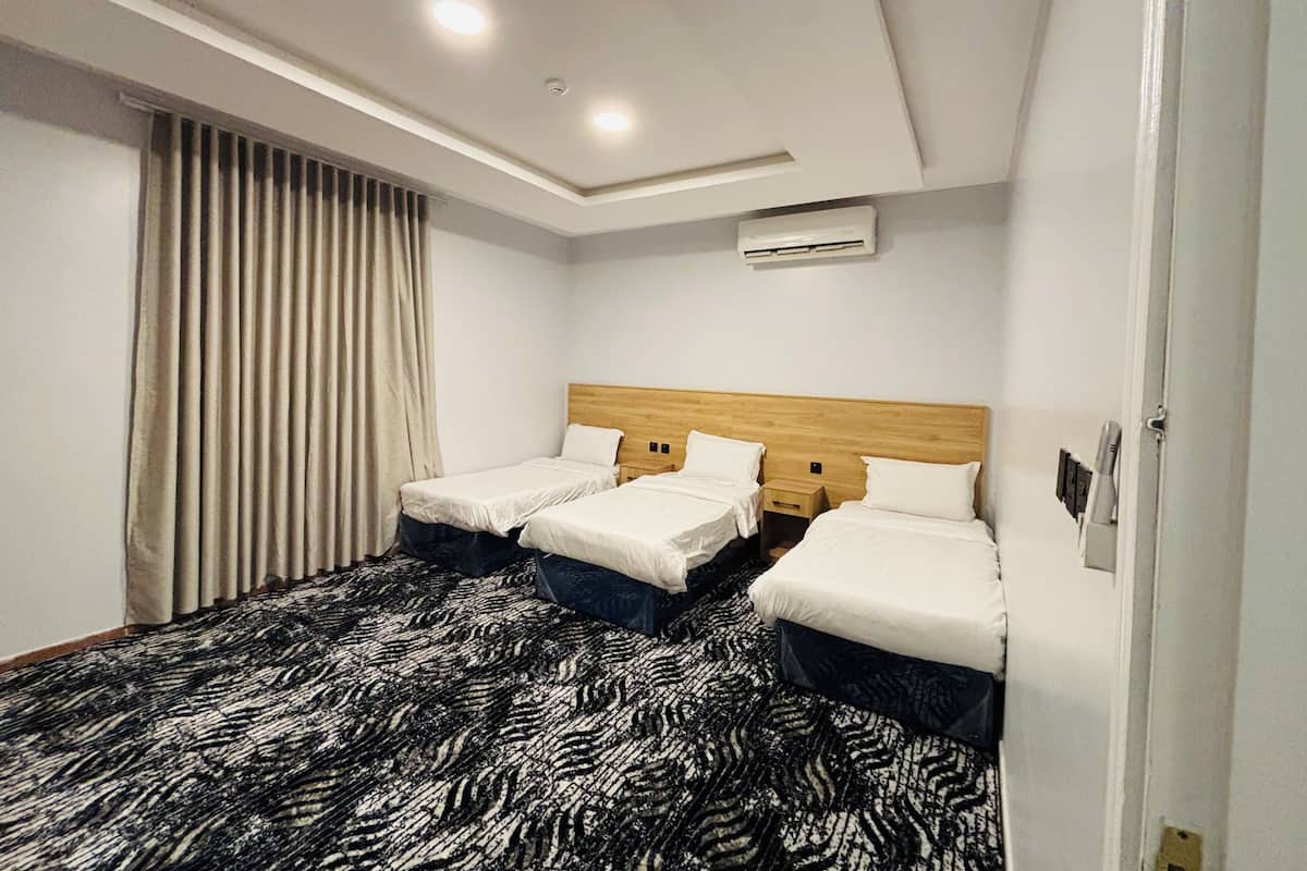 A hotel room with two beds, a patterned carpet, a ceiling light, and an air conditioning unit.
