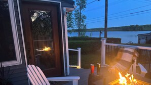 En terrasse med pejse, en hvid stol og udsigt til et sø.