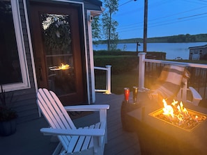 Une terrasse avec un foyer, une chaise blanche et une vue sur un lac.