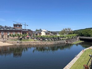 A riverside hotel with stone walls, a bridge, and a grassy area with parked motorcycles.