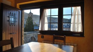 Un comedor con mesa y sillas, una ventana con cortinas y vistas a una iglesia y un puente.