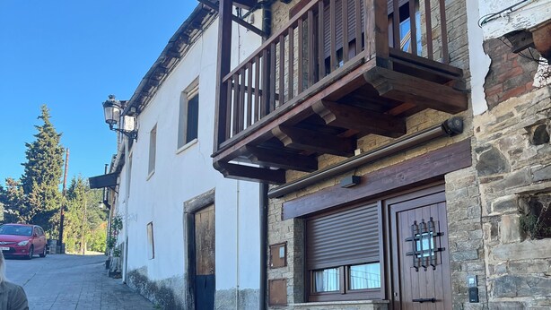 Un edificio tradicional con fachada de piedra, balcón de madera y una puerta con contraventana cerrada.