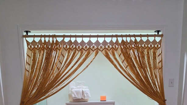 Una stanza con un'armadio bianco, un piccolo tavolo con una candela e una tenda decorativa in macramè.