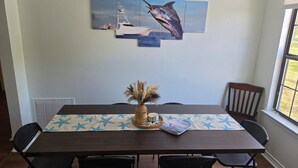Un tavolo da pranzo con una tovaglia a motivi stellati, un vaso intrecciato con piante secche e un quadro con un pesce.