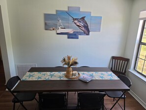 Ein Esstisch mit Tischdecke mit Sternenmuster, eine gewebte Vase mit getrockneten Pflanzen und ein gerahmtes Kunstwerk von einem Fisch.