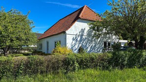 Un edifici blanc amb teulada vermella, envoltat de vegetació i arbres.