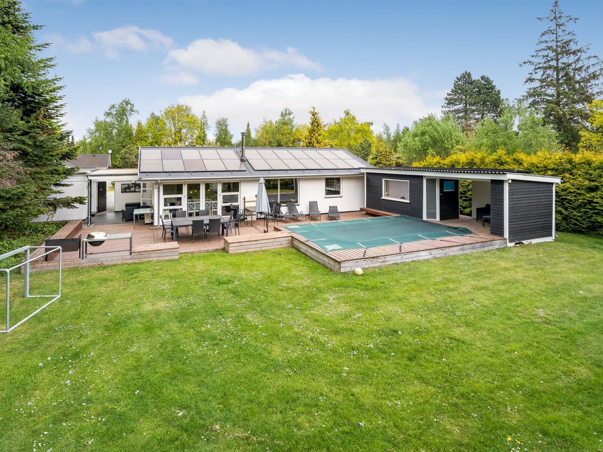 Une maison moderne dotée d’un patio couvert, d’une piscine et d’un jardin clôturé.