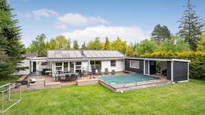Et moderne hus med en overdækket terrasse, swimmingpool og en lukket have.