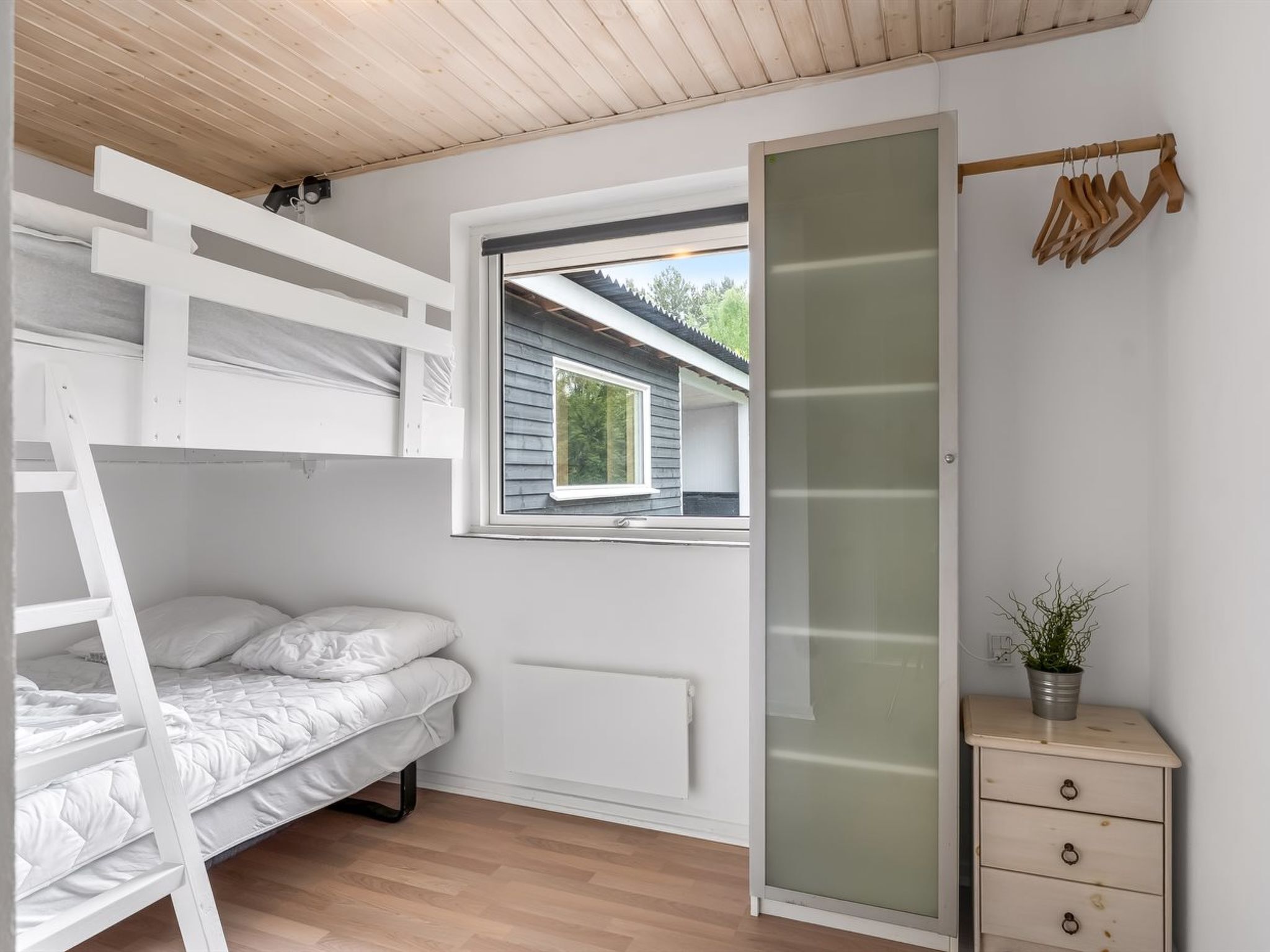 A bedroom with a bunk bed, a window, a radiator, a dresser, and a plant.