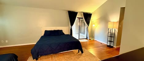 A bedroom with a bed, a nightstand, a lamp, and a view of a balcony.