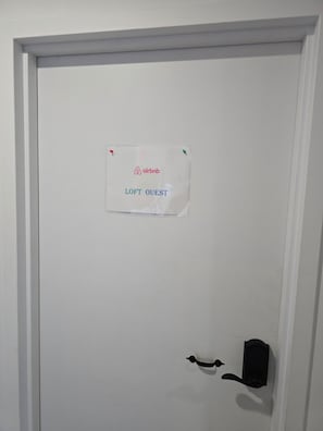 Eine weiße Tür mit einem Schild, das angibt, dass es sich um ein Airbnb namens 'LOFT OUEST' handelt.