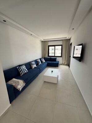 A modern living room with a sectional sofa, a coffee table, and a flat-screen TV mounted on the wall. - Cozy Flat Sea & Hills View | Smir Hill (Marina Smir)