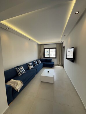 A modern living room with a sofa, a coffee table, and a TV mounted on the wall. - Cozy Flat Sea & Hills View | Smir Hill (Marina Smir)