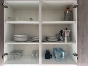 A white cabinet with shelves containing plates, glasses, and a coffee maker. - Cozy Flat Sea & Hills View | Smir Hill (Marina Smir)