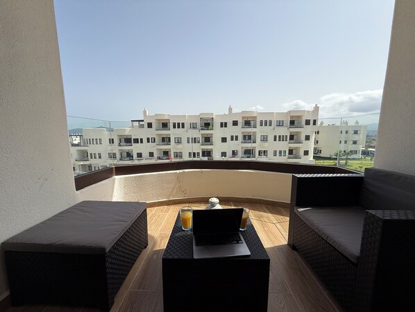 A balcony with wicker furniture, a laptop, and a glass of orange juice. - Cozy Flat Sea & Hills View | Smir Hill (Marina Smir)