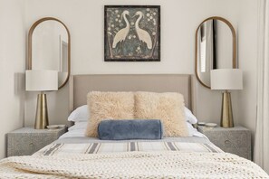 A bed with a beige headboard, two fluffy pillows, a knitted blanket, and two bedside tables with lamps. - Vista Nest | Hill Country Views • Hot Tub Retreat (Canyon Lake)