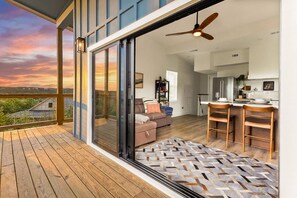 A modern interior with a wooden deck, a sofa, a dining area, and a kitchen. - Vista Nest | Hill Country Views • Hot Tub Retreat (Canyon Lake)