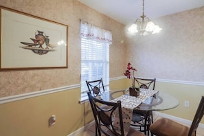 A dining room with a round table, chairs, a chandelier, a window with blinds, and a framed picture on the wall. - Relax at The Pelican Perch, a stylish 2-bedroom, 2-bath condo/apt in Gautier (Gautier)