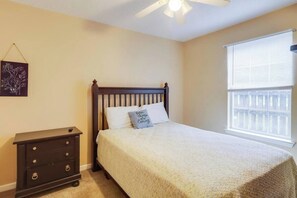 A bedroom with a bed, a nightstand, a ceiling fan, a window with blinds, and a wall-mounted artwork. - Relax at The Pelican Perch, a stylish 2-bedroom, 2-bath condo/apt in Gautier (Gautier)