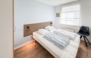 A bedroom with a wooden headboard, a bed with white and blue bedding, a black chair, and a window with sheer curtains. - Pet friendly home in Gråsten with sauna (Gråsten)
