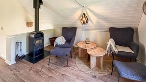 Ein gemütlicher Raum mit Kaminofen, zwei Sesseln, einem runden Holztisch und einer Pendelleuchte.
