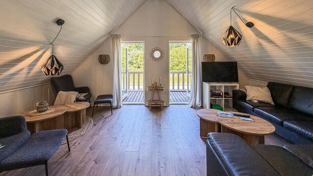 Ein gemütliches Loft-Wohnzimmer mit hohen Decken, Holzböden, einem schwarzen Ledersofa, einem Holztisch und einem Fernseher auf einem weißen Schrank.