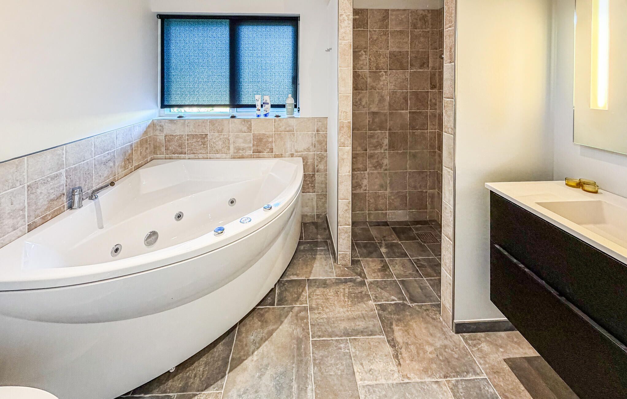 A modern bathroom with a freestanding bathtub, a window with blue blinds, and a shower area.