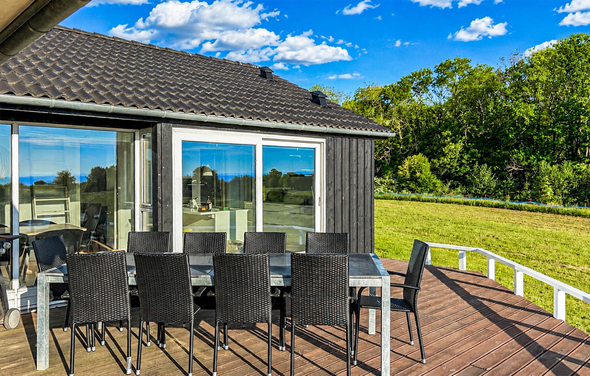 A deck with outdoor furniture, a glass door leading to a patio, and a view of a green landscape.