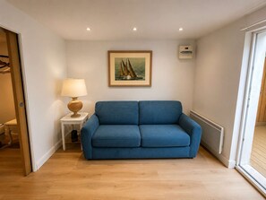 A room with a blue sofa, a small table with a lamp, a framed picture on the wall, and a window. - A cozy vacation home with a terrace (PYLA SUR MER)