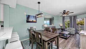 A dining area with a wooden table and chairs, a ceiling fan, and a view through large windows. - Treasure Island Gulf Front Condo Ocean Views (Treasure Island)