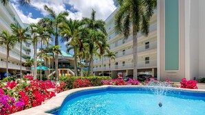 A hotel with a swimming pool surrounded by palm trees and vibrant flowers. - Treasure Island Gulf Front Condo Ocean Views (Treasure Island)