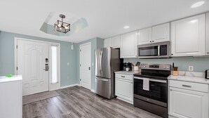 A modern kitchen with white cabinets, stainless steel appliances, and a wooden floor. - Treasure Island Gulf Front Condo Ocean Views (Treasure Island)