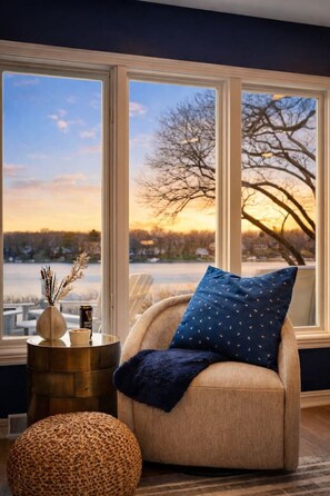 Ein gemütlicher Raum mit großem Fenster, einem Sessel, einem kleinen Beistelltisch und einem gewebten Hocker.