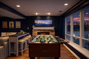 Una habitación con mesa de futbolín, televisor sobre la chimenea y sofá.