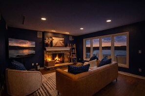 Ein gemütliches Wohnzimmer mit Kamin, einem großen Fenster mit Blick auf ein Gewässer und einer komfortablen Sitzecke.