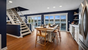 Et moderne køkken med en central ø, et spiseområde med udsigt og en trappe til en balkon.