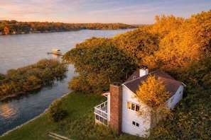 Ein Haus mit Backsteinkamin, weißer Fassade und einem Balkon mit Blick auf einen Fluss.